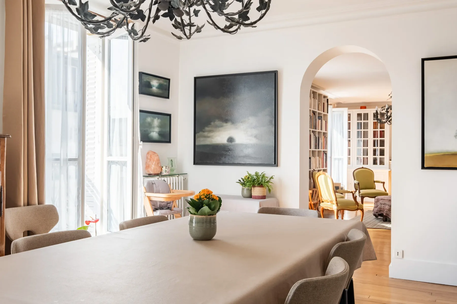 A bright dining area with a long table and an arched opening to a sitting room.