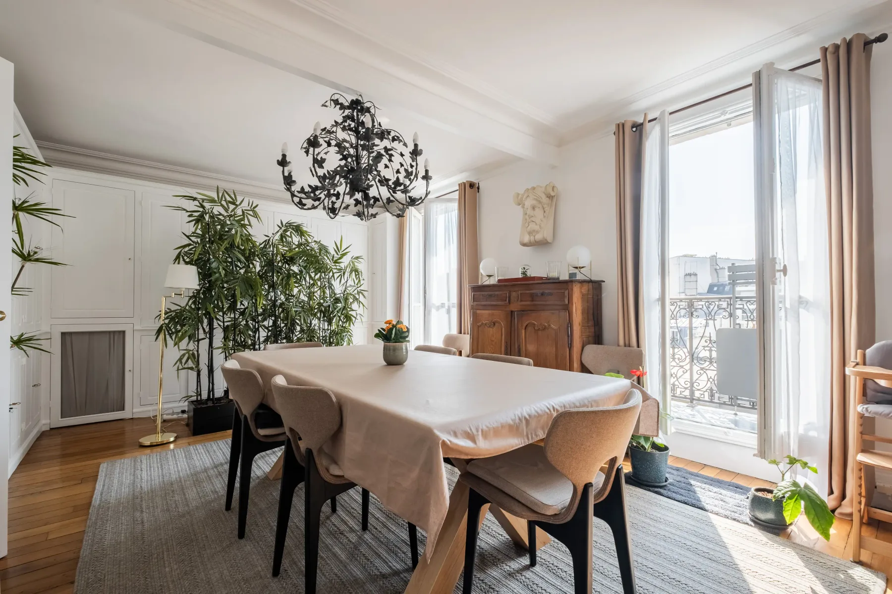 A bright dining room with a long table and tall windows opening onto a balcony.