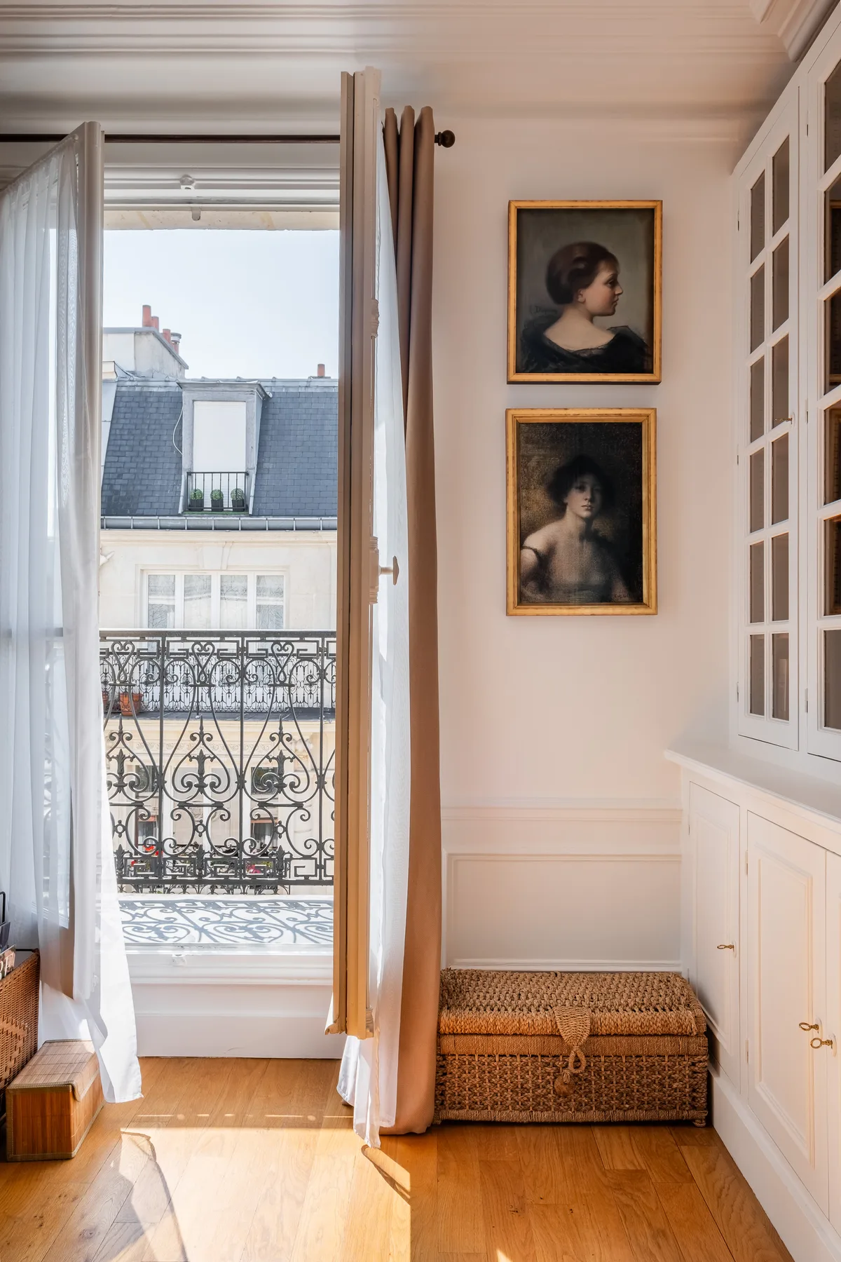 A bright room opens onto a balcony, with framed portraits above a woven chest.