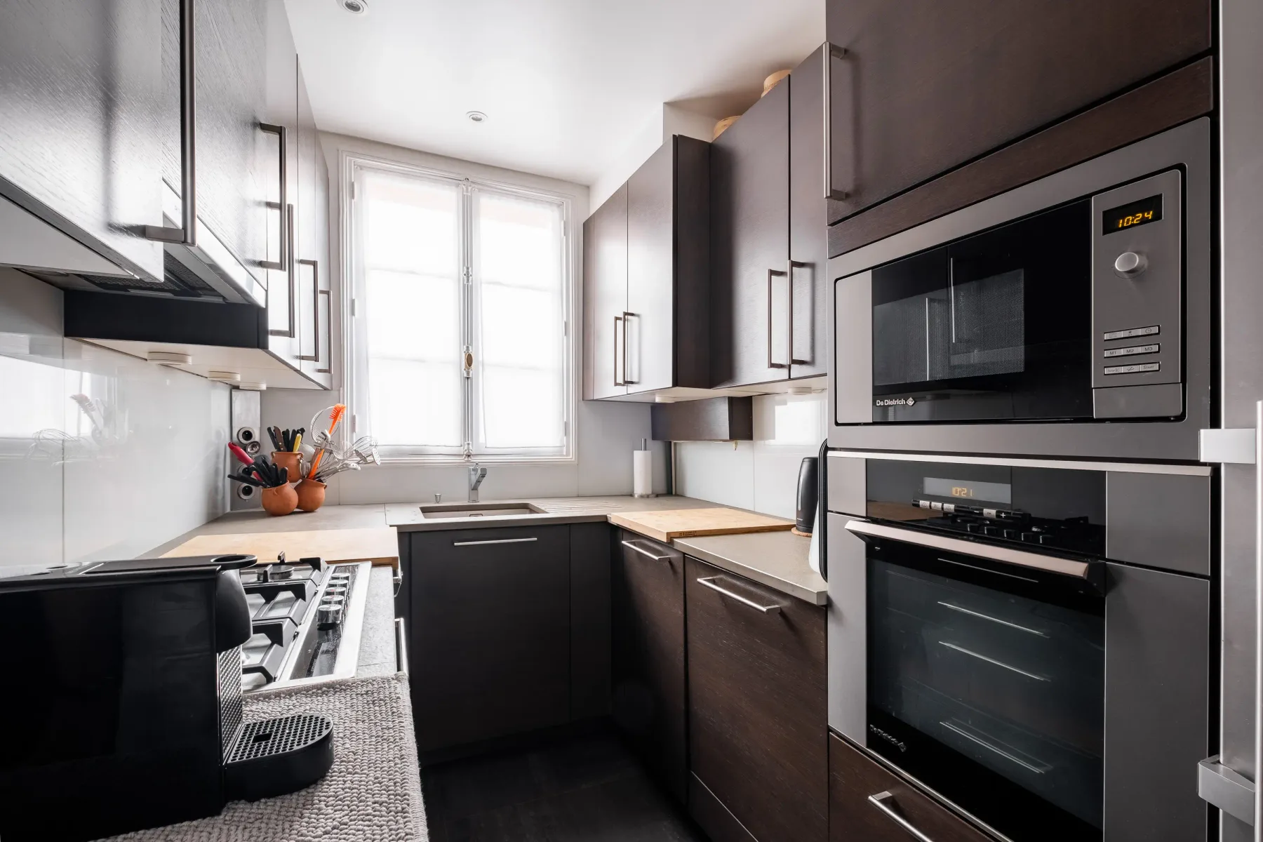 A modern kitchen with dark cabinetry, light countertops, and built-in appliances.