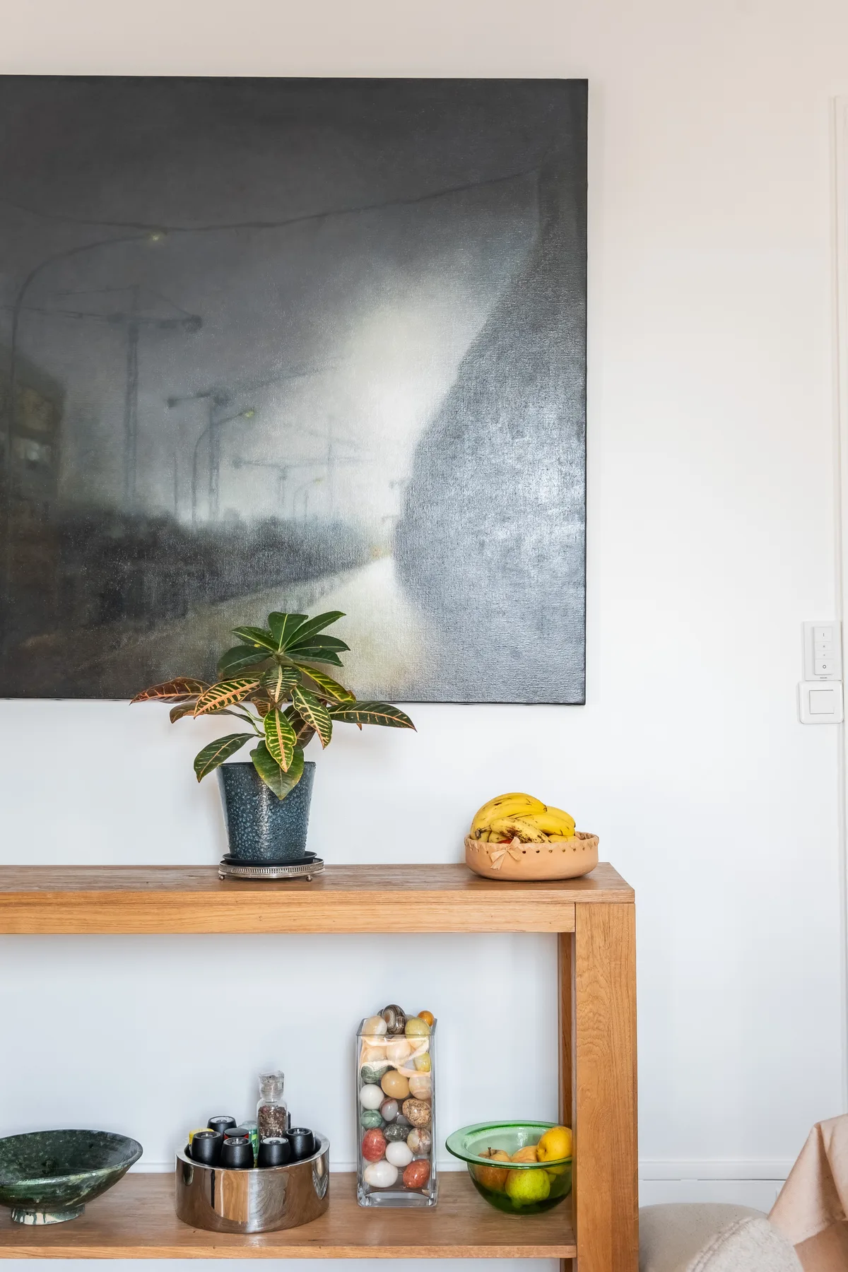 A wooden console table displays a potted plant, bowls, and a large abstract painting.
