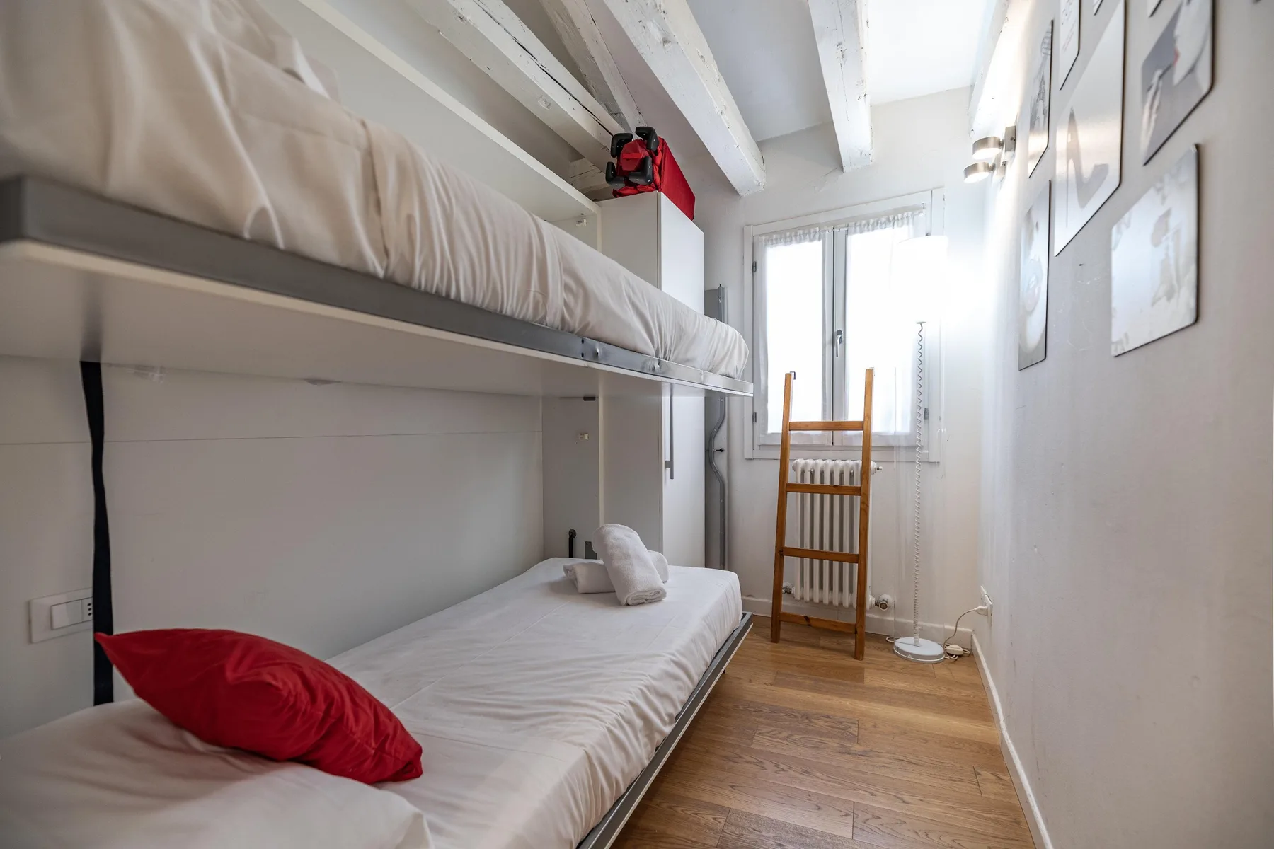 Un dormitorio compacto con literas, ropa de cama blanca y cuadros en la pared.