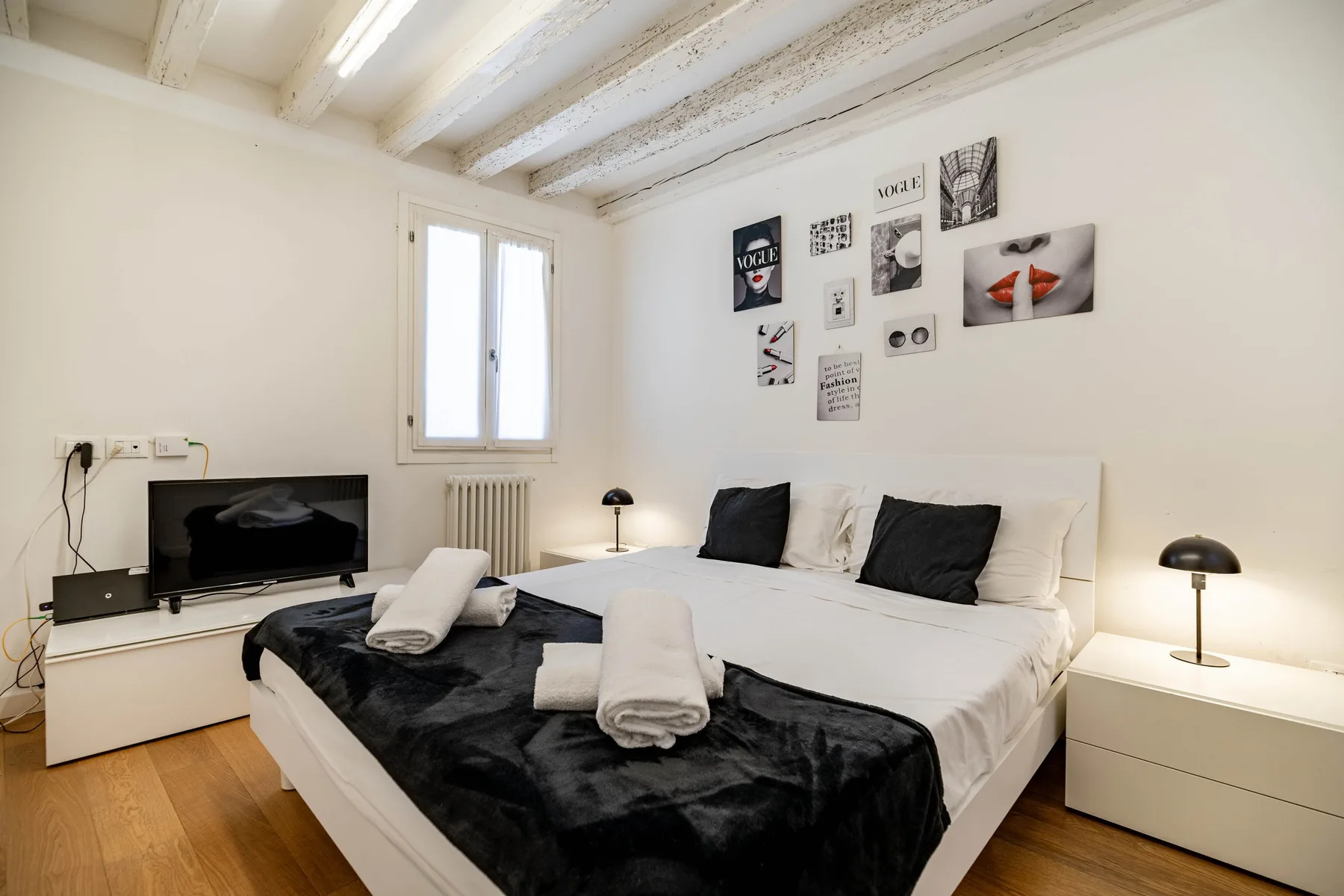 Un dormitorio luminoso con una cama, una manta oscura y cuadros en la pared.