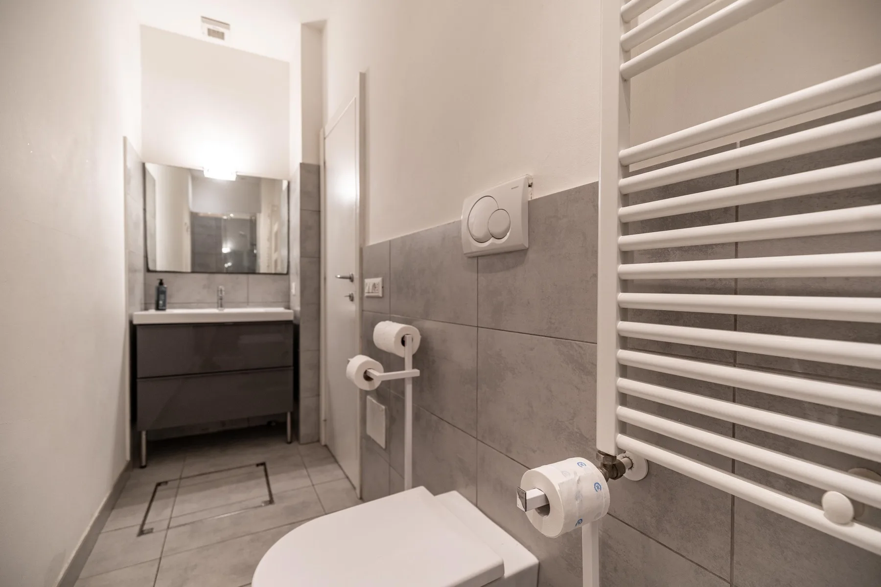 Un baño con lavabo suspendido, espejo y toallero calefactable.