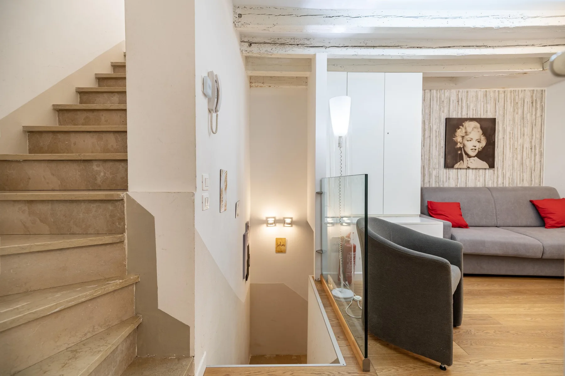 Una zona de estar con un sofá gris queda junto a una escalera y un panel de vidrio.