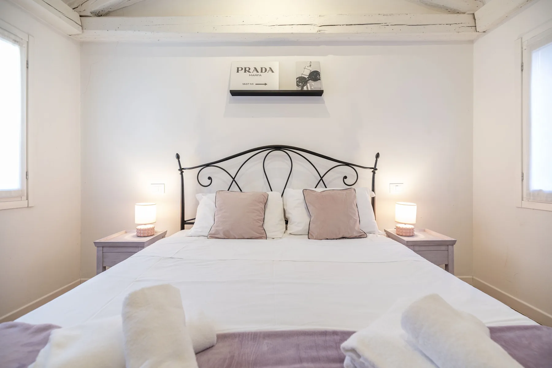 Un dormitorio luminoso con una cama de metal, ropa de cama blanca y mesitas de noche.