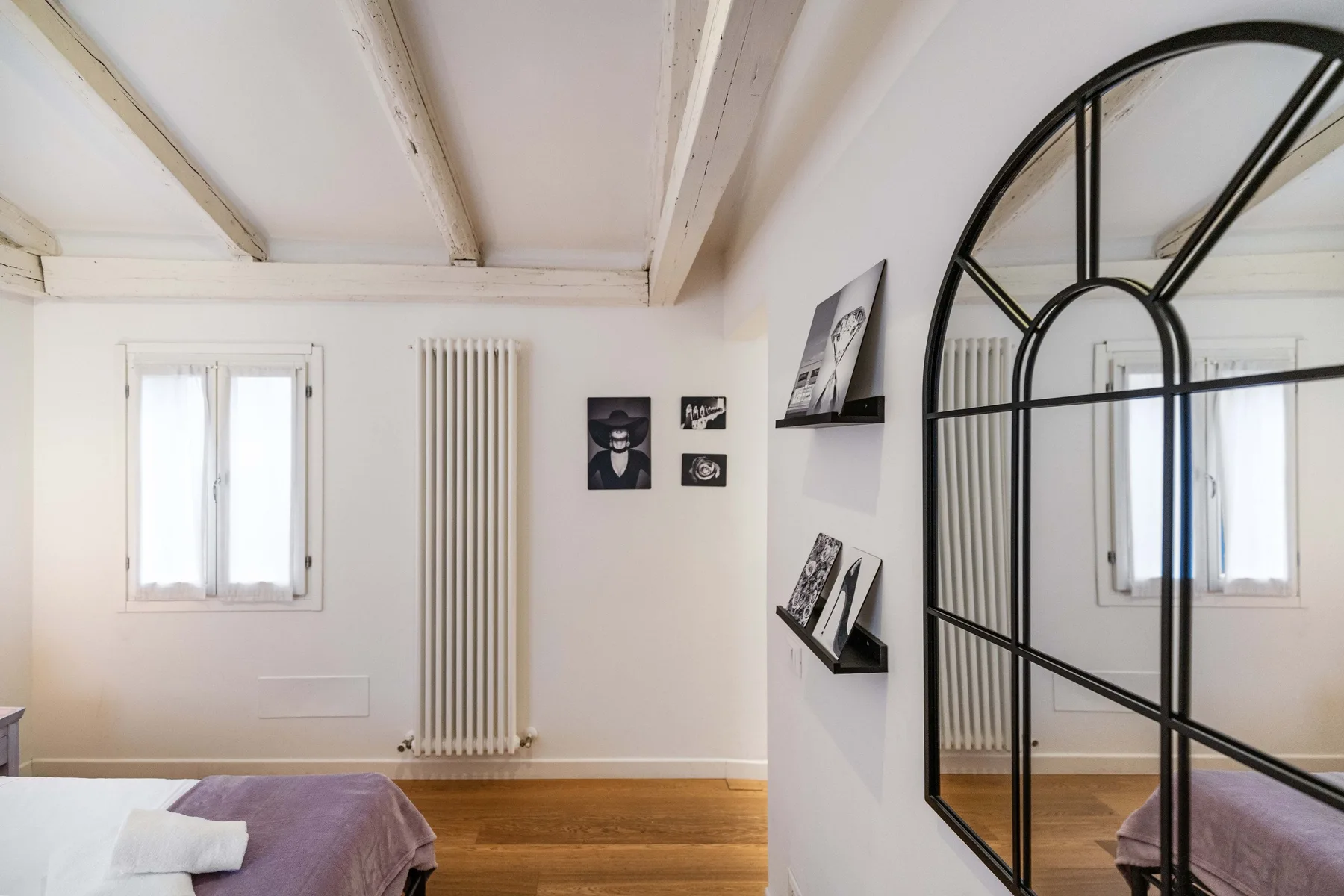 Un dormitorio luminoso con una cama, arte mural y un gran espejo arqueado.