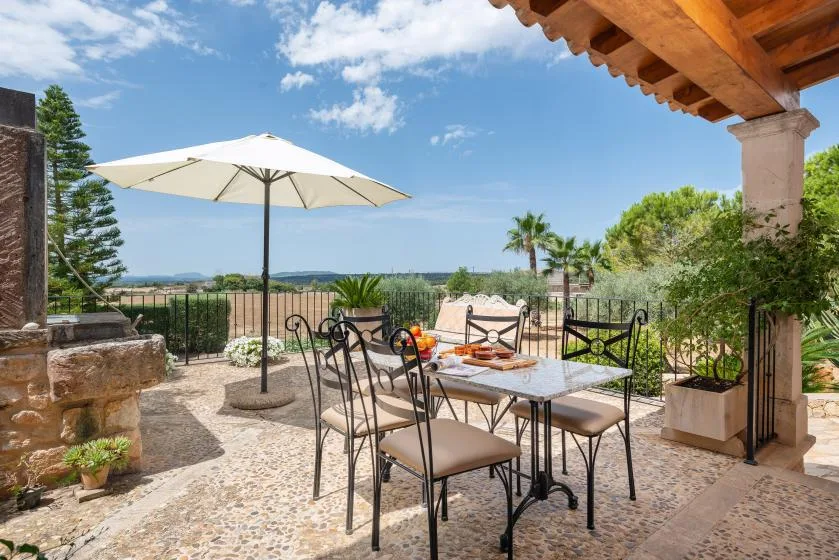 Un patio al aire libre con una mesa, asientos y una sombrilla grande.