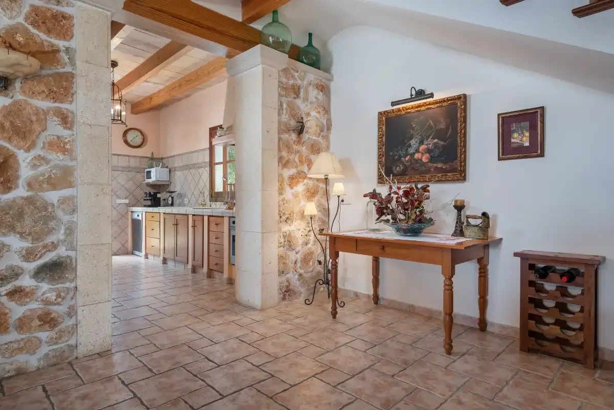 Una zona de comedor rústica se abre a la cocina, con suelo de baldosas y vigas vistas.