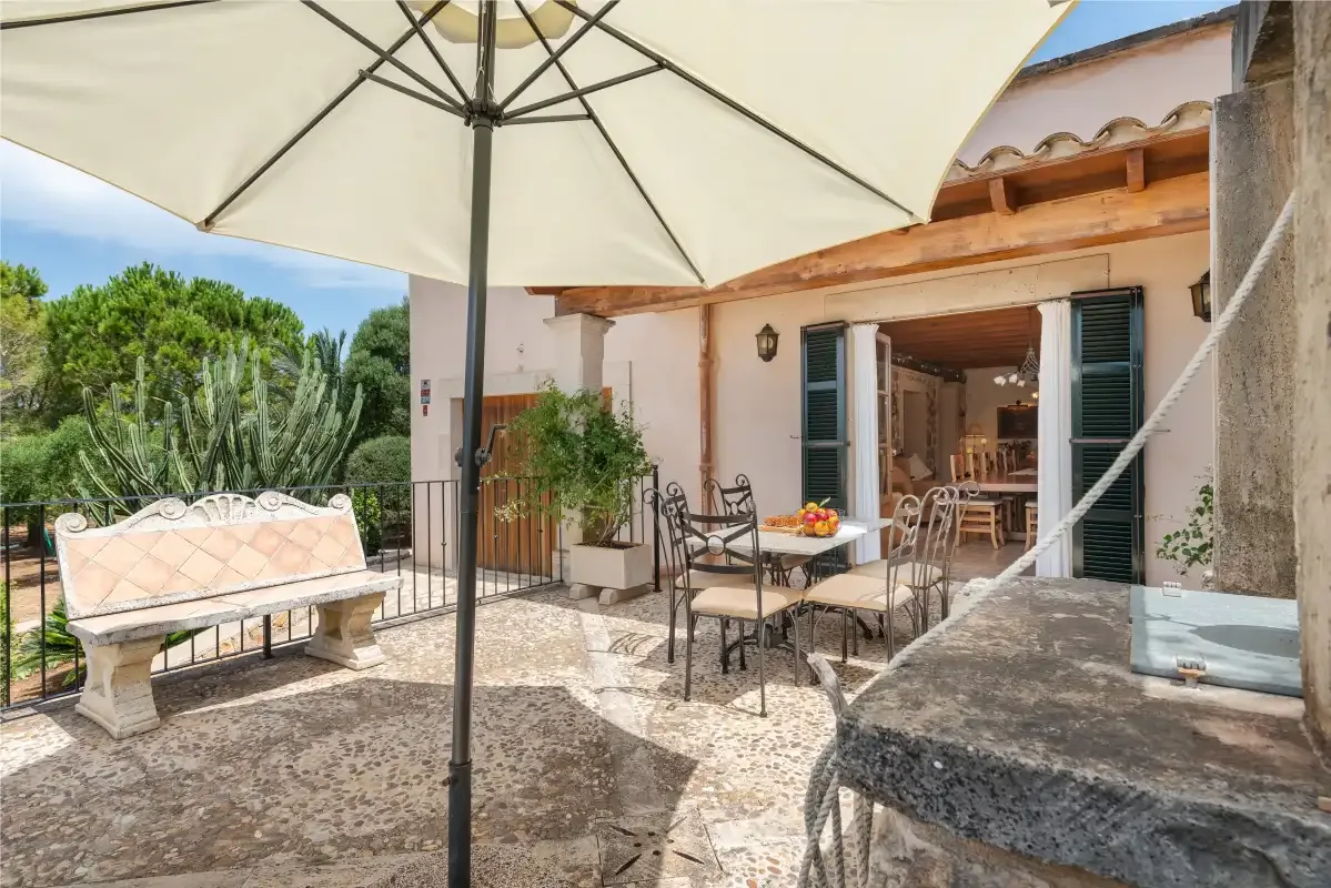 Un patio de piedra soleado con asientos al aire libre y una puerta abierta al comedor.