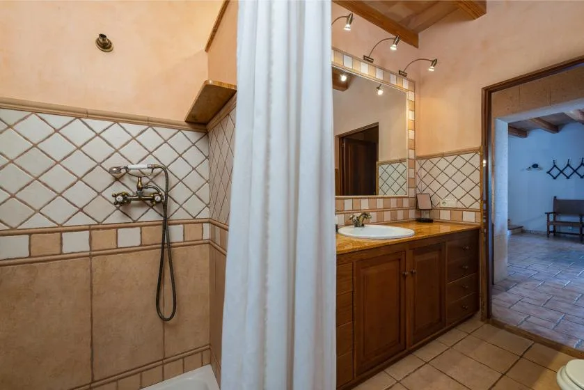 Un baño alicatado con ducha, lavabo y mueble de madera.