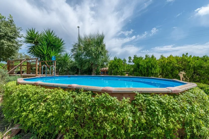 Una piscina al aire libre está rodeada de abundante vegetación bajo un cielo parcialmente nublado.