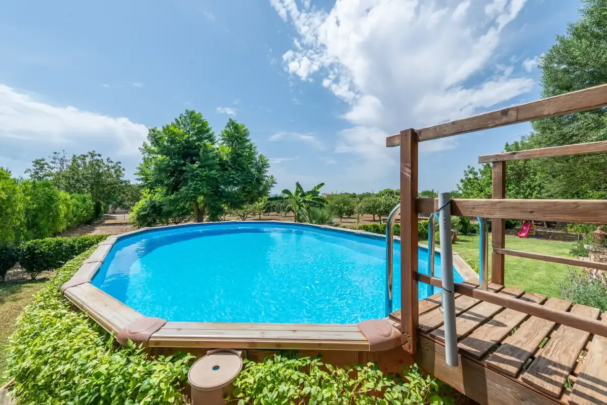 Una piscina exterior está junto a una terraza de madera y un jardín verde.