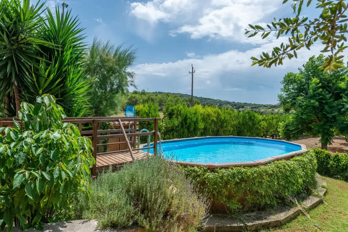 Una piscina está rodeada de vegetación frondosa bajo un cielo parcialmente nublado.