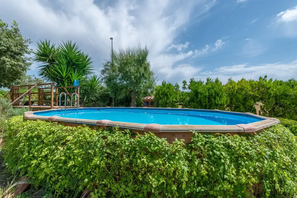 Una piscina al aire libre está rodeada de vegetación bajo un cielo parcialmente nublado.