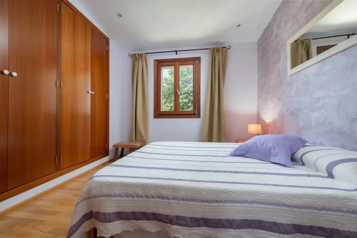 Dormitorio con una colcha a rayas y una ventana enmarcada por cortinas.