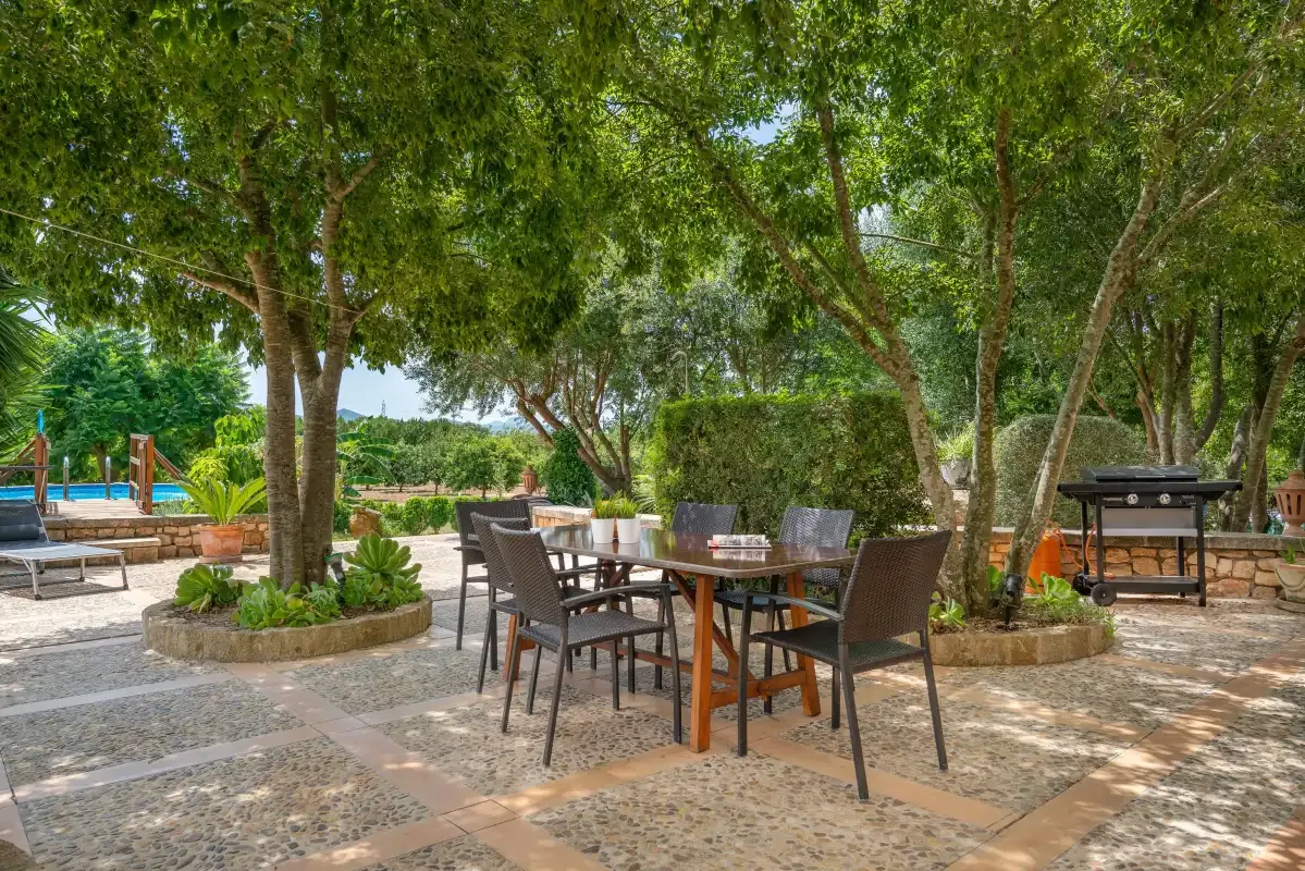 Una zona de comedor exterior a la sombra de árboles está junto al jardín y la piscina.
