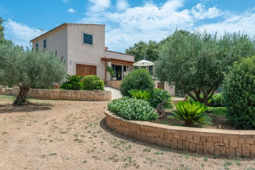 Una casa se alza detrás de parterres ajardinados y árboles maduros.
