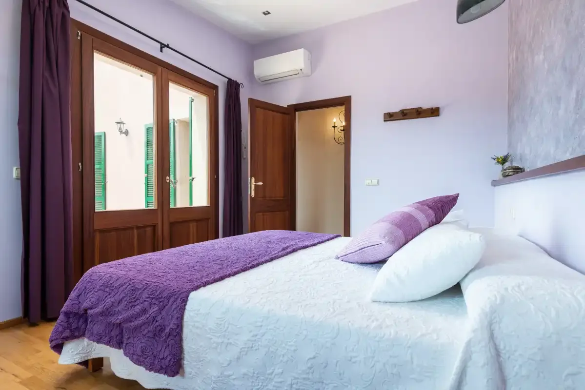 Un dormitorio con una cama cubierta con ropa de cama blanca y morada.