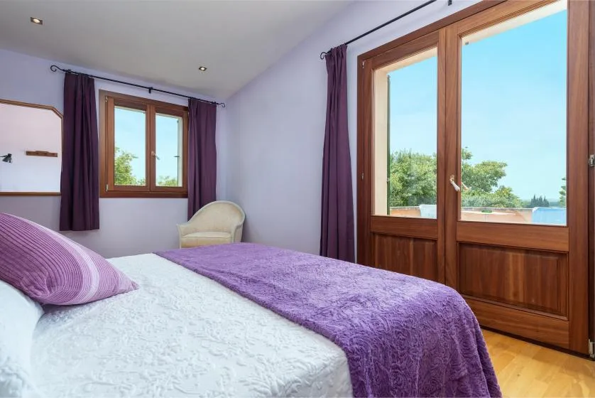 Un dormitorio con una cama cubierta de ropa de cama morada junto a grandes puertas acristaladas.