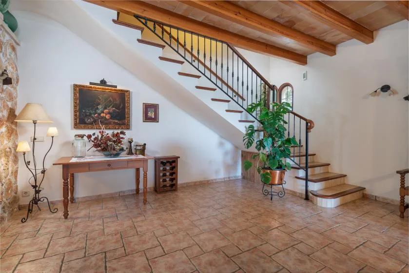 Interior con suelo de baldosas, escalera de madera, mesa consola y planta en maceta.