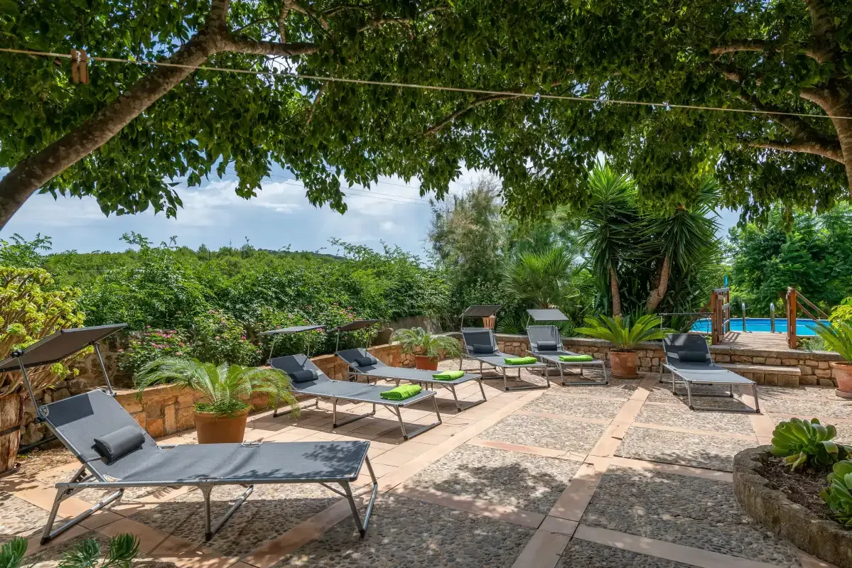 Un patio exterior sombreado tiene asientos para relajarse y una piscina al fondo.