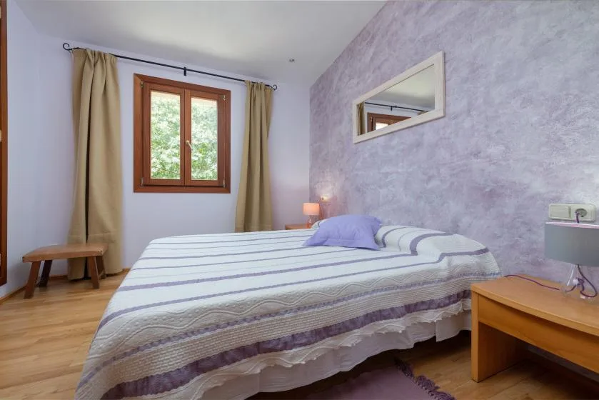 Un dormitorio con una colcha a rayas, una ventana de madera y mesitas de noche.