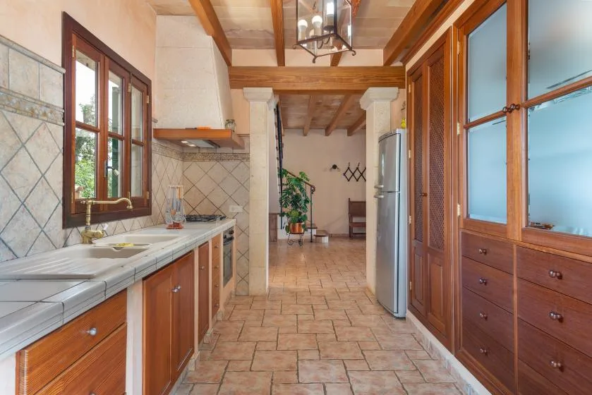 Una cocina alargada con gabinetes de madera, encimeras de azulejos y un refrigerador.