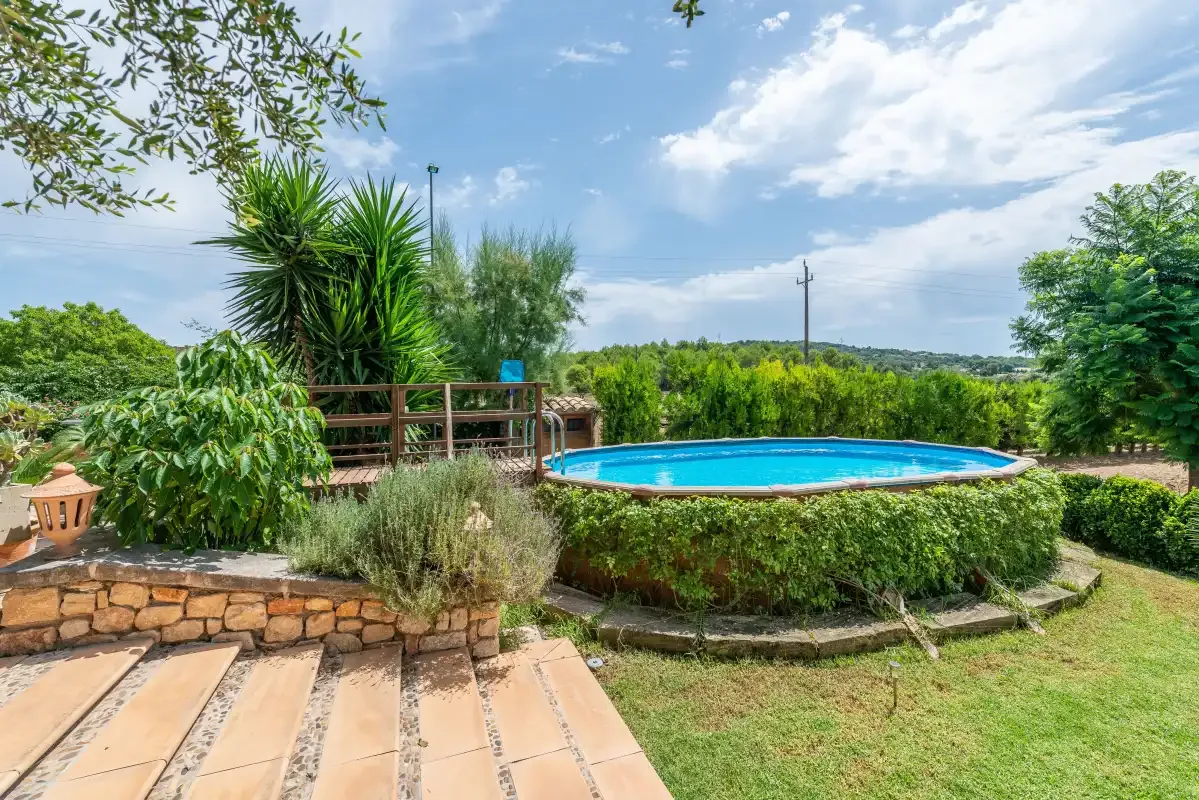 Una piscina al aire libre está rodeada de vegetación junto a un sendero pavimentado.