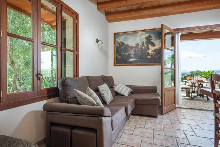 Una sala de estar con asientos marrones, ventanales y una puerta abierta a una terraza.