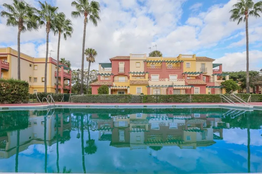 A swimming pool reflects colorful buildings and palm trees.