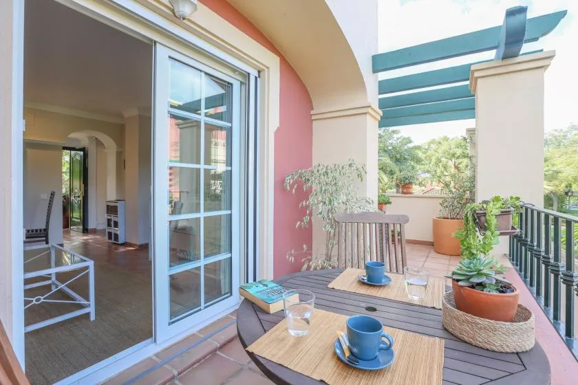 A covered outdoor patio with a table, seating, and potted plants.
