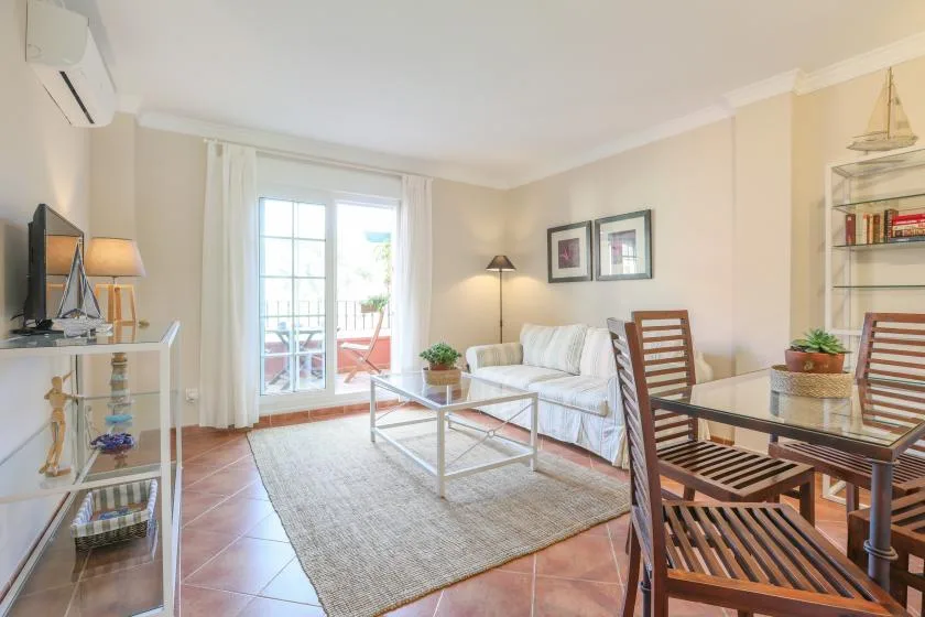 A bright living room with seating, a coffee table, and glass doors opening to a balcony.