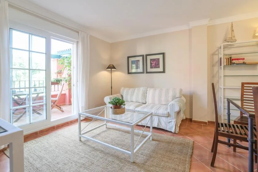 A bright living room with a striped sofa, glass coffee table, and balcony doors.