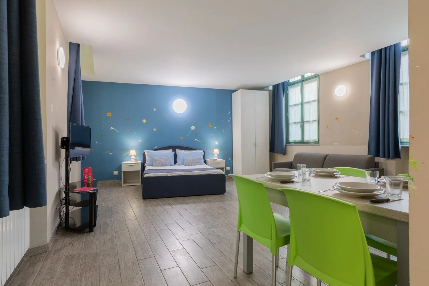 Un dormitorio con una cama junto a una mesa de comedor y sillas verdes.