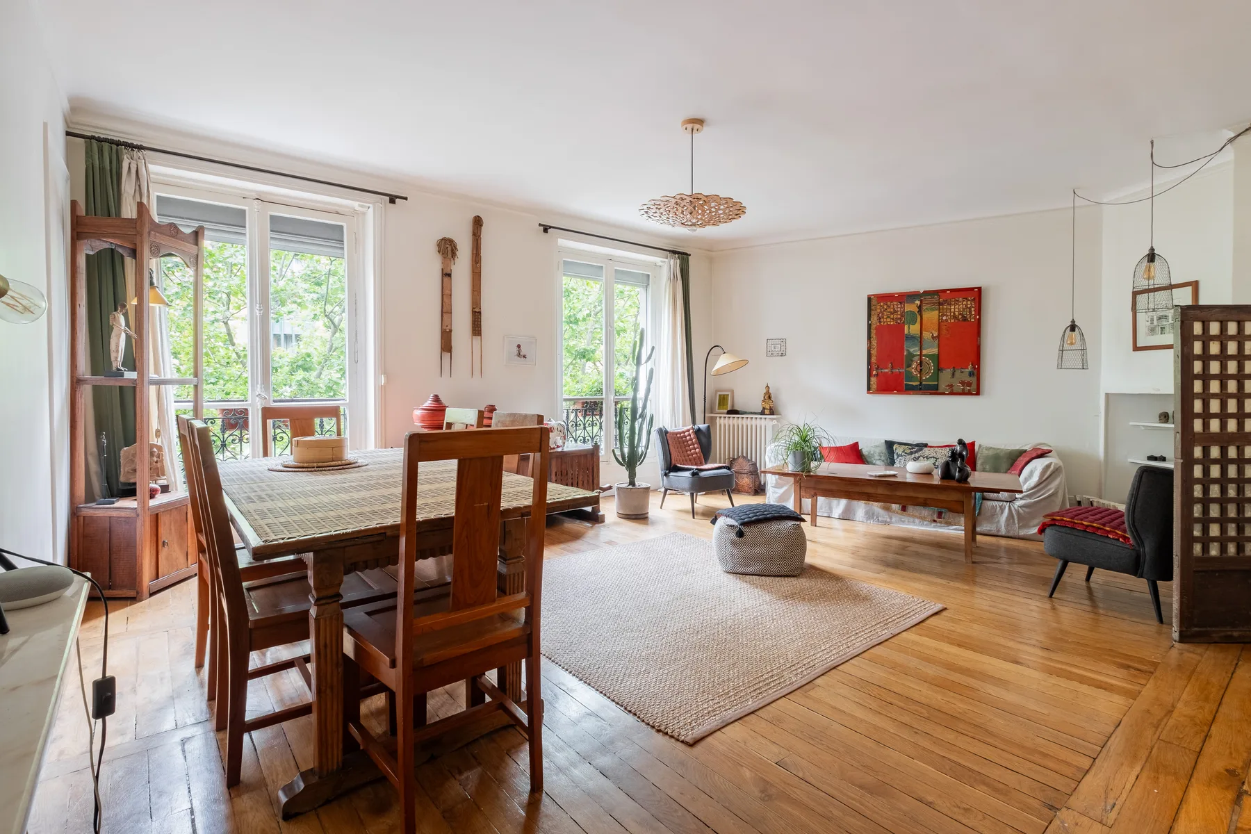 A bright living and dining room has wooden seating, a rug, and large windows.