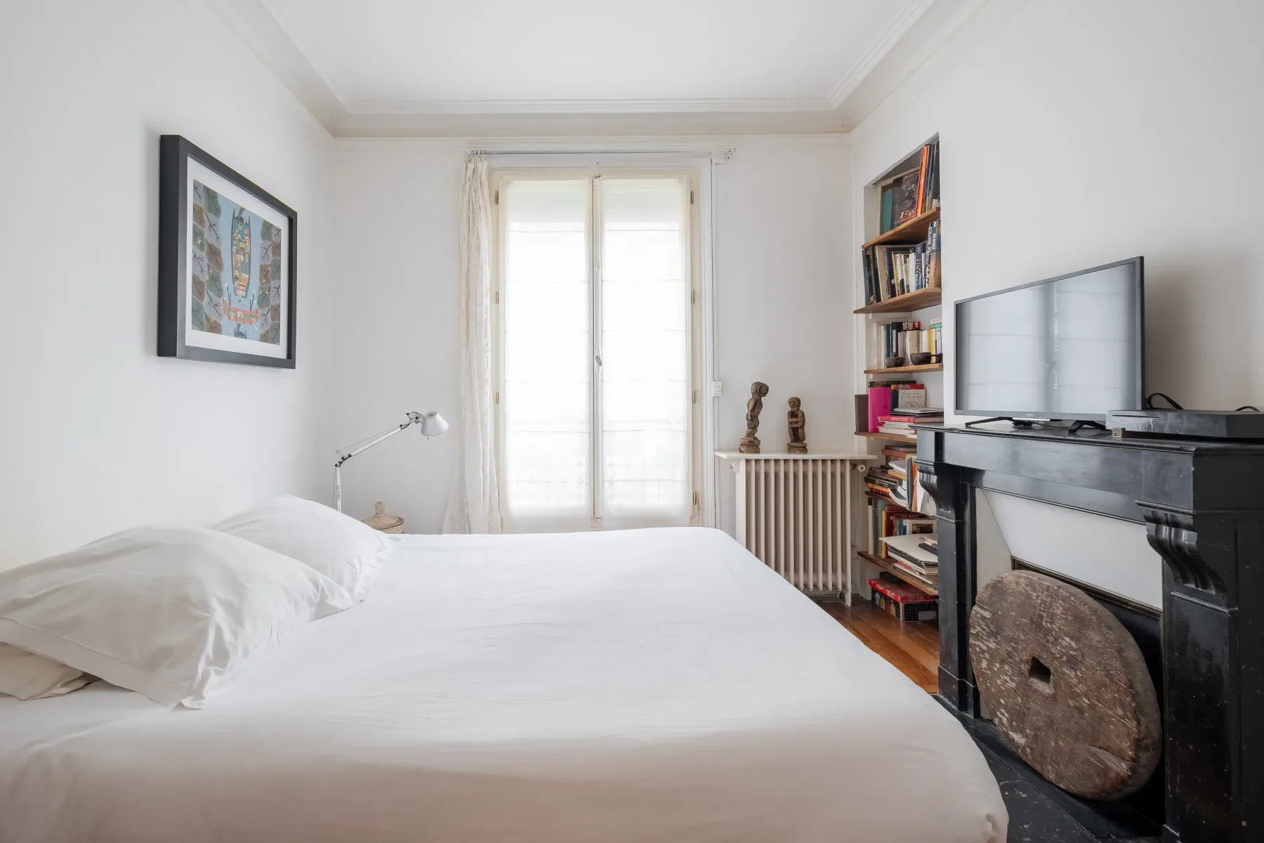 A bright bedroom with a neatly made bed and a television on the mantel.