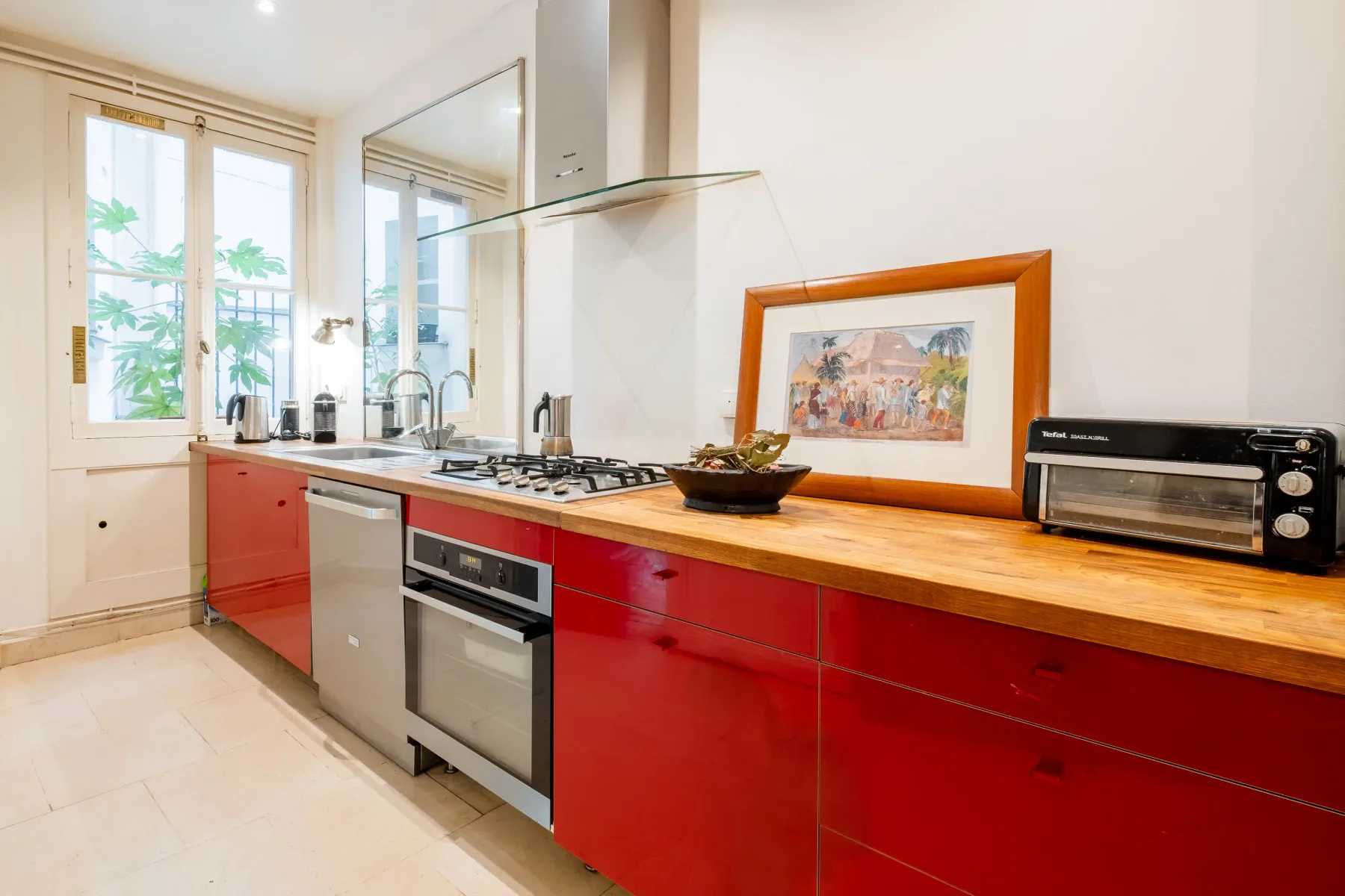A bright kitchen with red cabinets, a countertop, and a window.
