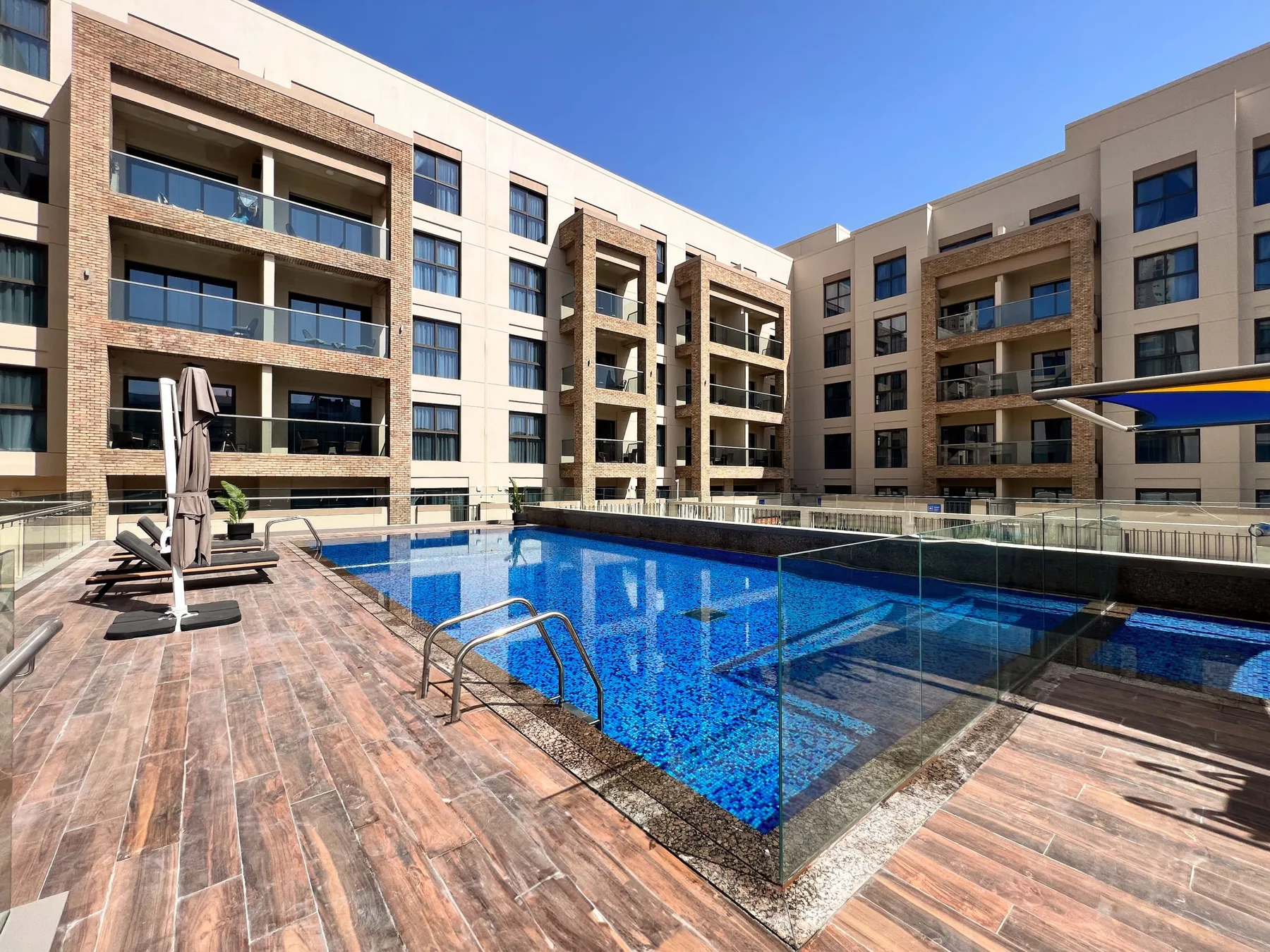 Una piscina al aire libre está junto a un edificio de varios pisos y una terraza.