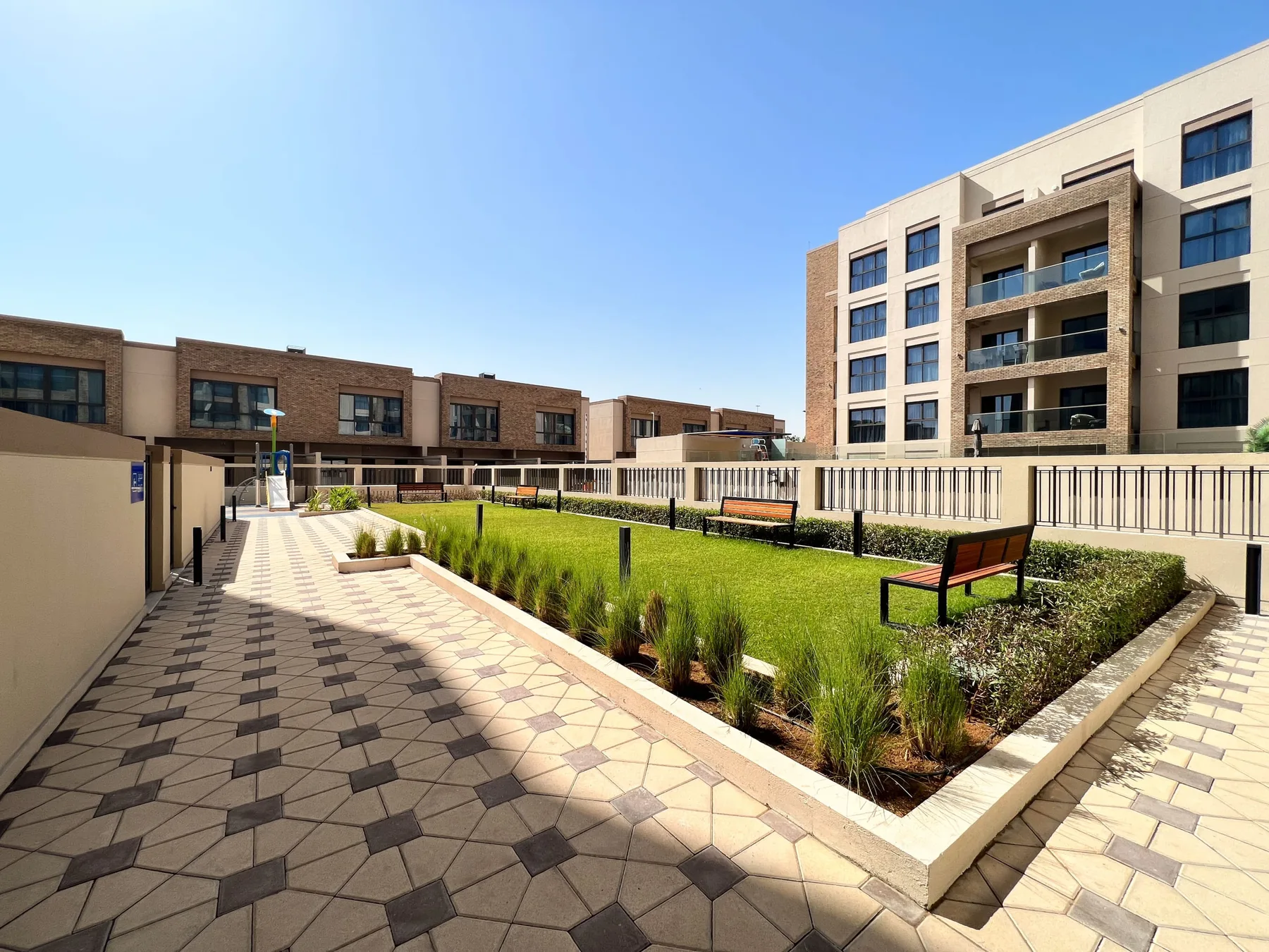 Un patio ajardinado tiene senderos pavimentados, césped verde y edificios de apartamentos alrededor.
