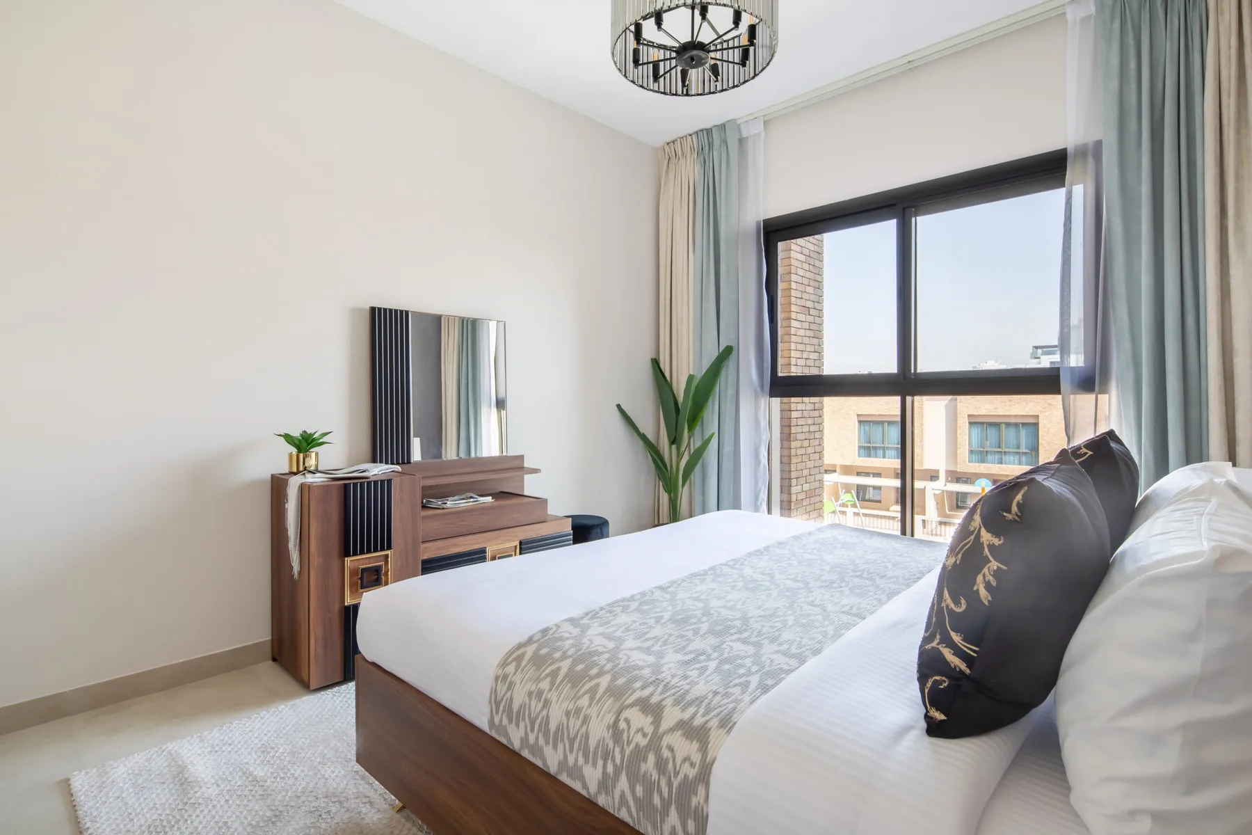 Un dormitorio luminoso con una cama, una ventana grande y un televisor sobre una cómoda.