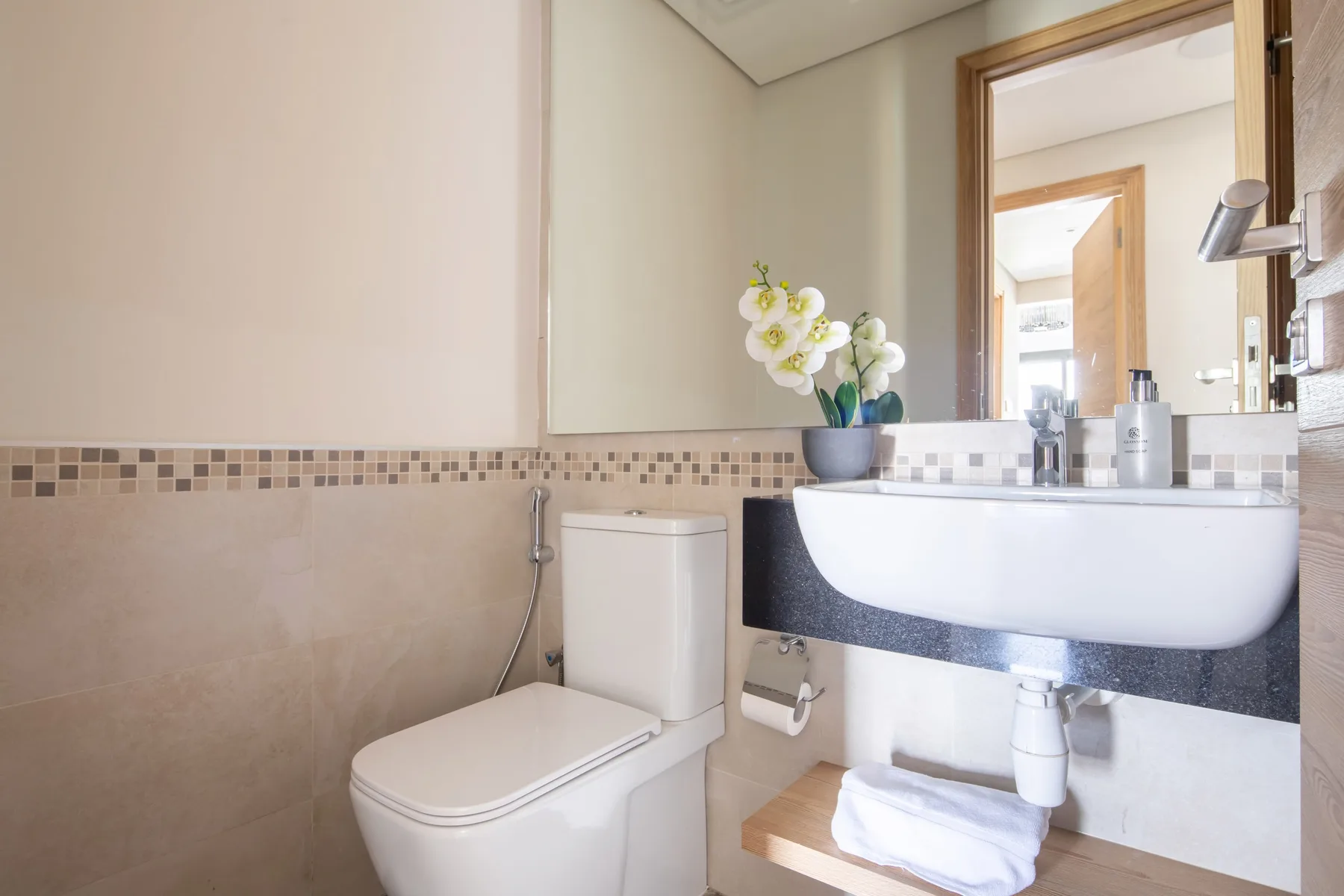 Un baño con inodoro, lavabo mural y una orquídea.