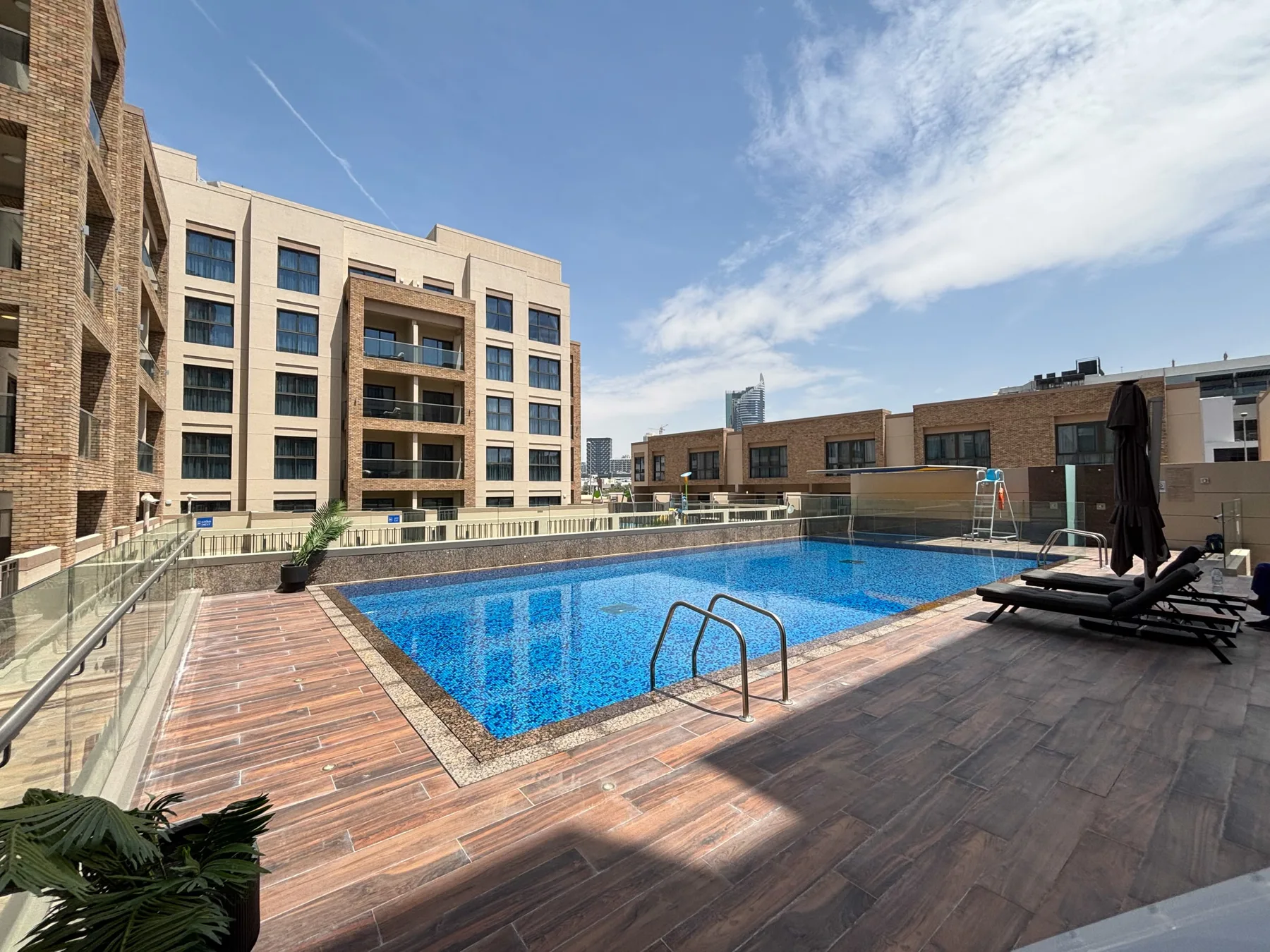 Una piscina en la azotea está rodeada por una terraza de tonos madera y edificios cercanos.