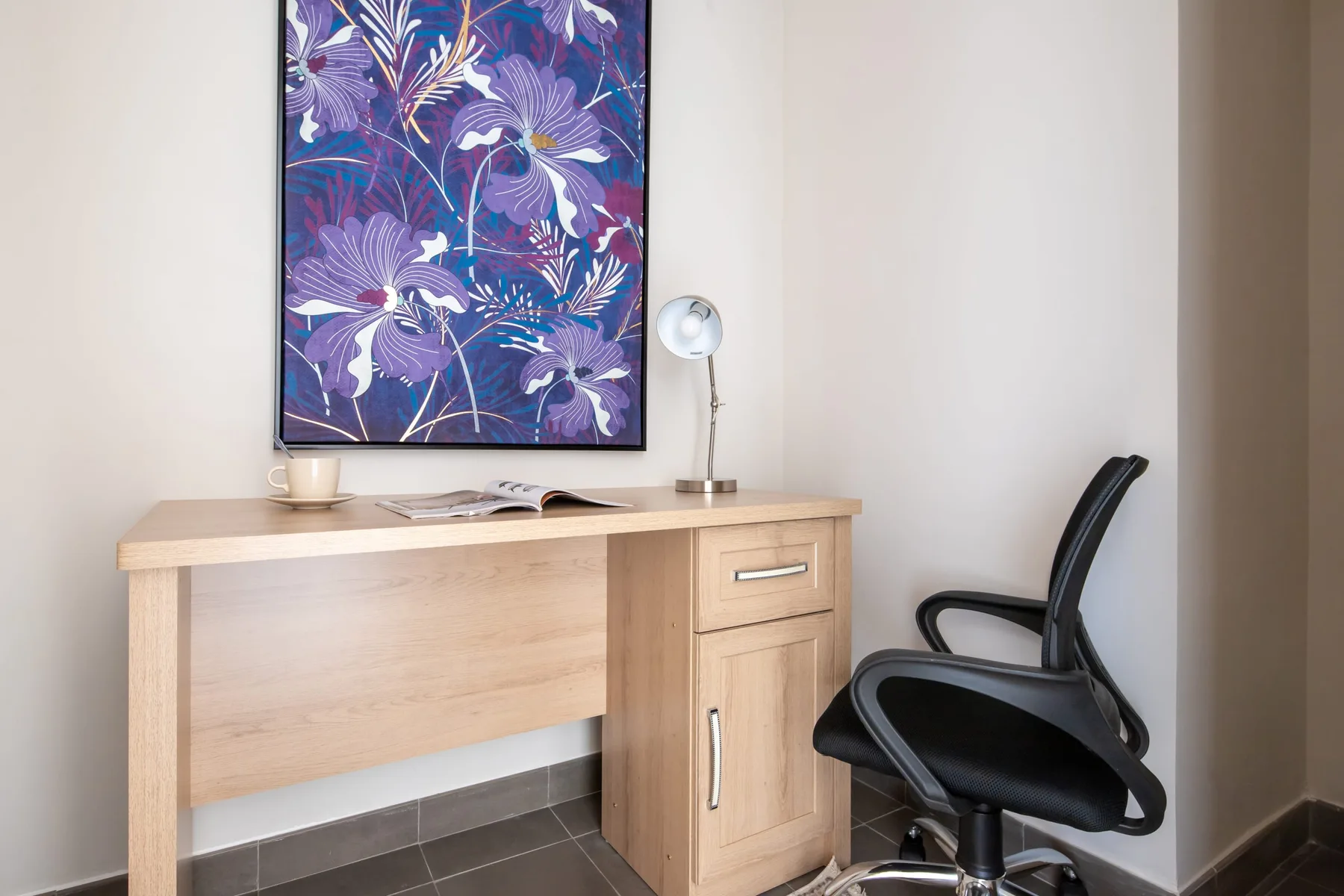 Un escritorio y una silla de oficina están bajo un cuadro floral colorido.