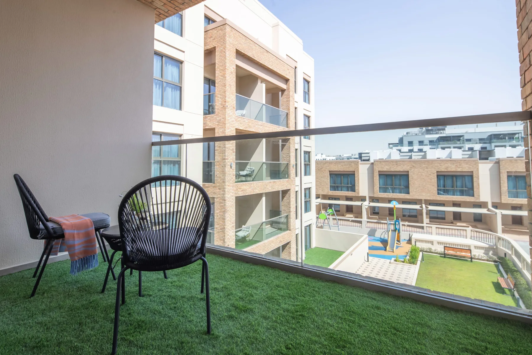 Un balcón con asientos al aire libre da a un patio y edificios cercanos.