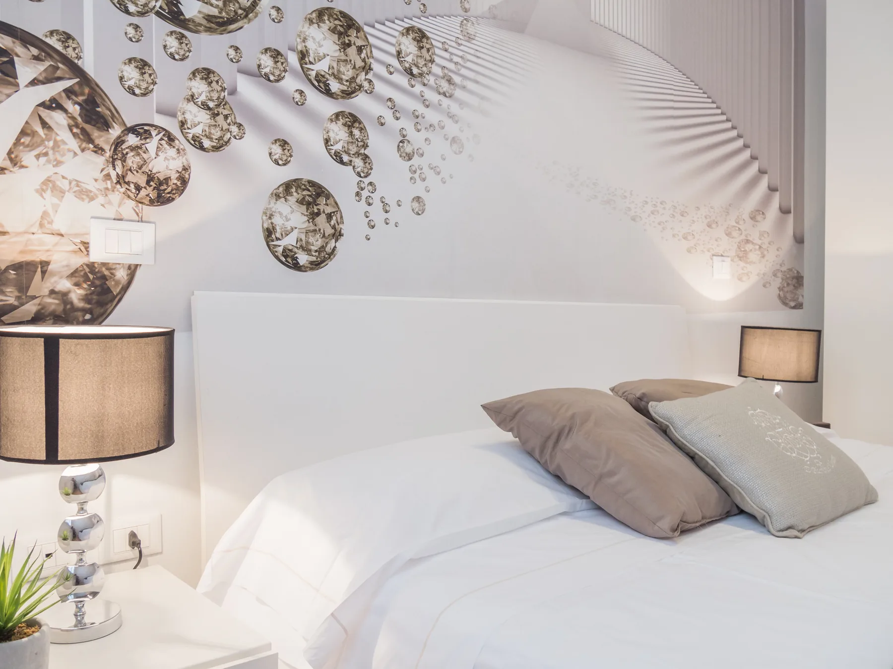 Un dormitorio con una cama blanca, arte decorativo en la pared y lámparas de noche.