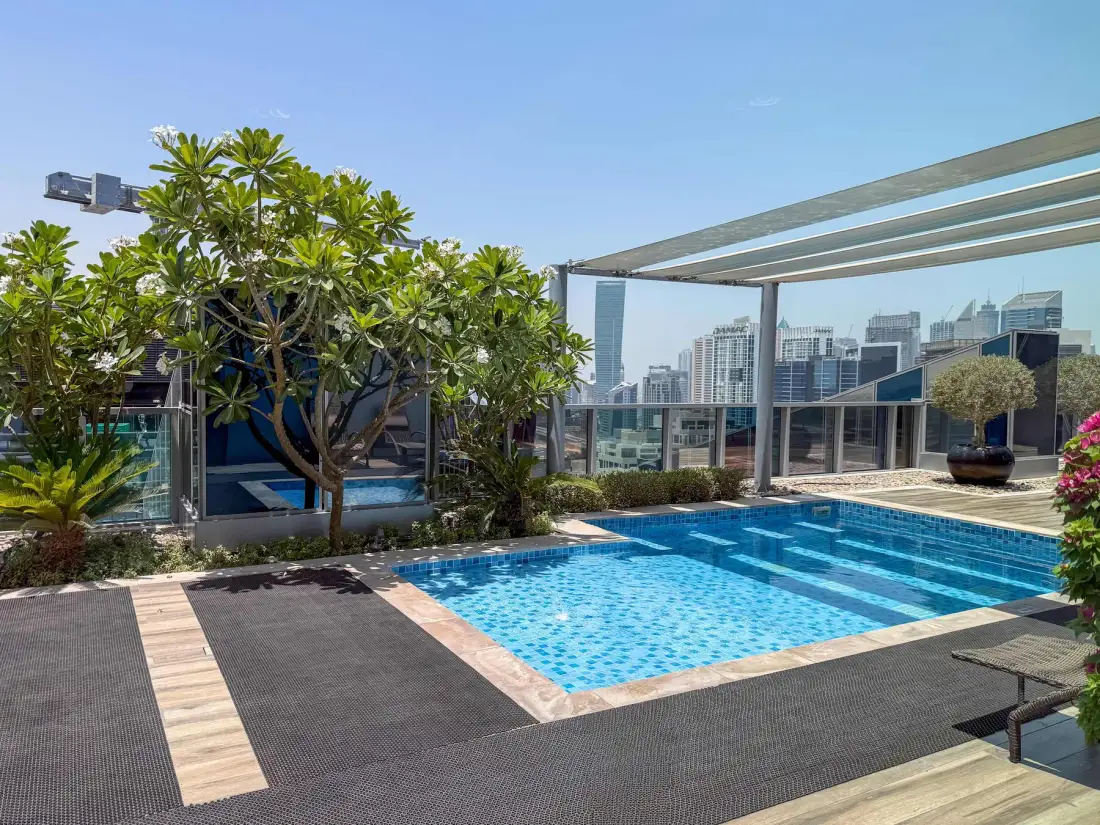 Una piscina en la azotea junto a árboles frondosos y una vista urbana acristalada.