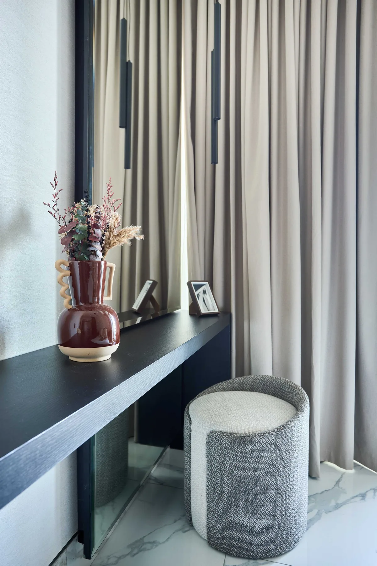 Una ventana con cortinas junto a una consola oscura y un asiento tapizado.