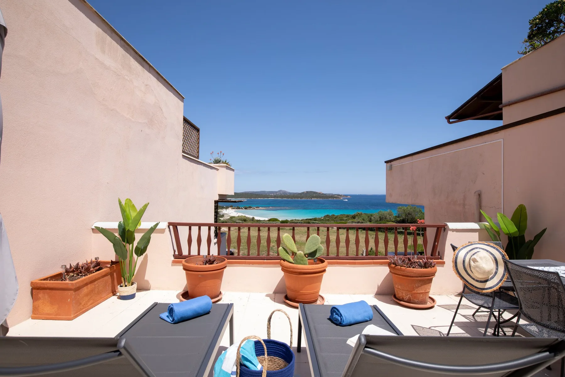 Una terraza soleada da al mar, con plantas en macetas y asientos al aire libre.