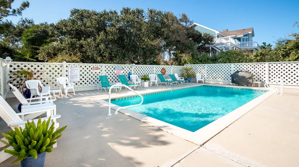 Una piscina al aire libre está rodeada de asientos y una cerca blanca de celosía.